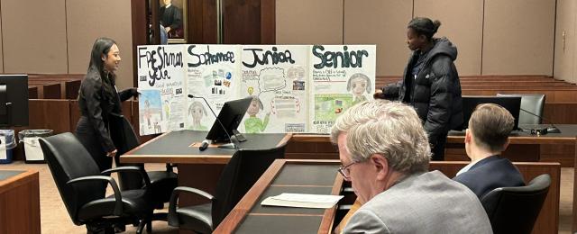 Students presenting proposal in front of panel group in a courtroom.